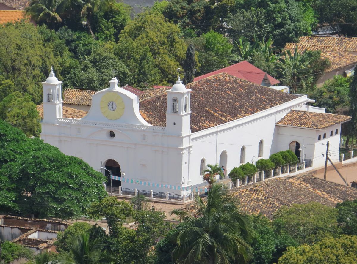Iglesia blanca de estilo colonial con techo de teja entre árboles